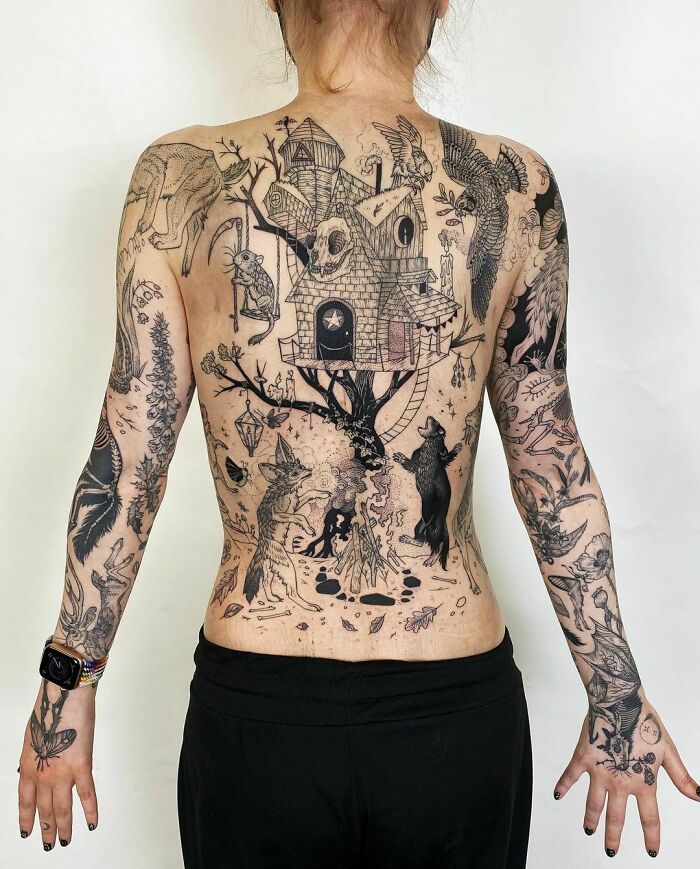 Spooky Halloween tattoos of haunted house and animals cover person's back and arms.