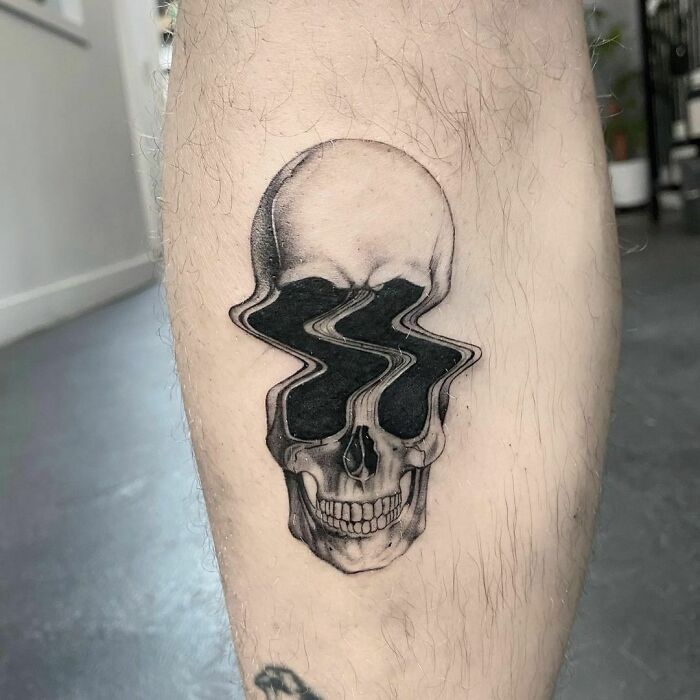 Spooky Halloween tattoo of a skull with distorted eye sockets on a person's leg.