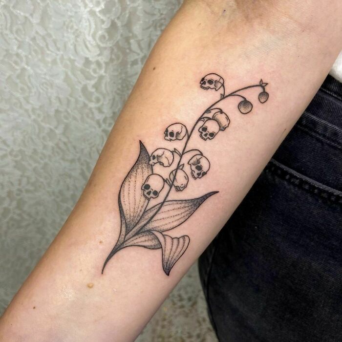 Spooky Halloween tattoo of a plant with skull-shaped blooms on forearm, blending botanical and horror elements intricately.
