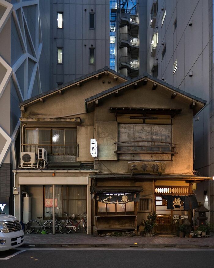 Old architecture in Japan with a traditional wooden house nestled between modern high-rise buildings at night.