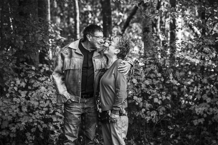 Couples in love sharing a tender moment outdoors surrounded by dense trees in a black and white photograph.