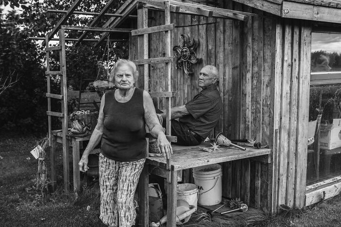 Black and white photo of an elderly couple outside a wooden shed, capturing love and companionship.