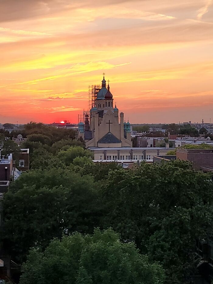 Sunset sky over a cityscape with a historic church and green trees capturing September weather conditions.