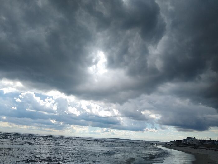 Dark storm clouds over the ocean shore with waves and distant beach houses showing September weather conditions.