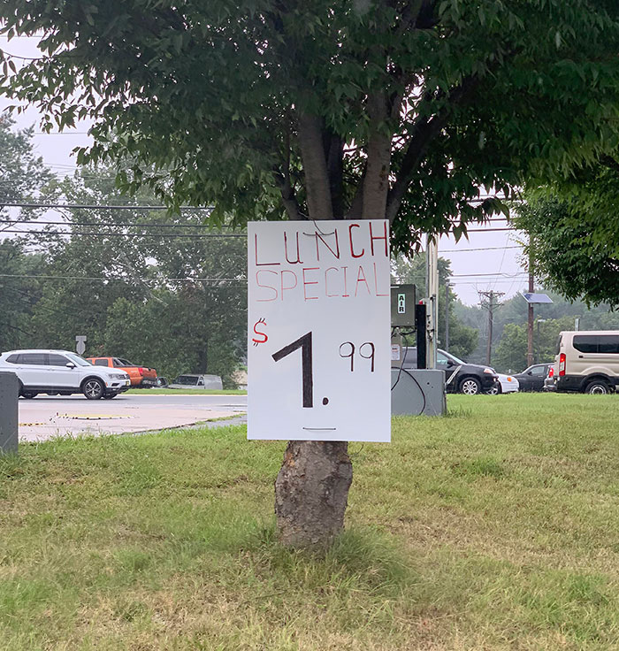 Handwritten lunch special sign on a tree at roadside illustrating evil marketing techniques in business pricing tactics.