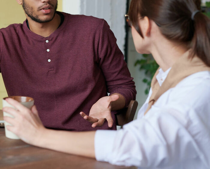 Man sharing disturbing facts to ruin your day while talking to a woman holding a mug at a wooden table indoors.