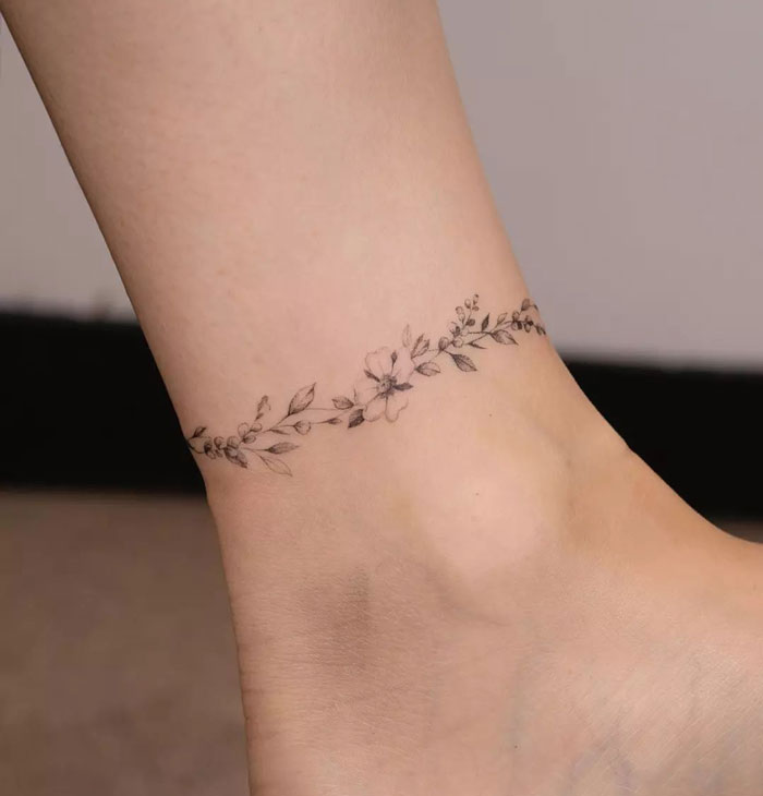 Delicate floral tattoo around an ankle showcasing a simple yet intricate first tattoo idea.
