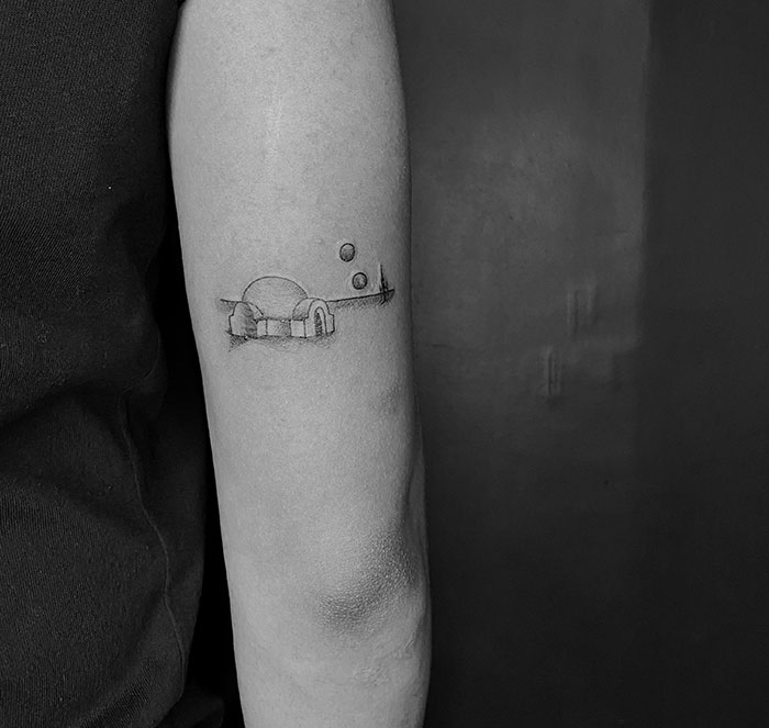 Minimalist space-themed first tattoo on forearm, featuring a dome and planets in black ink.