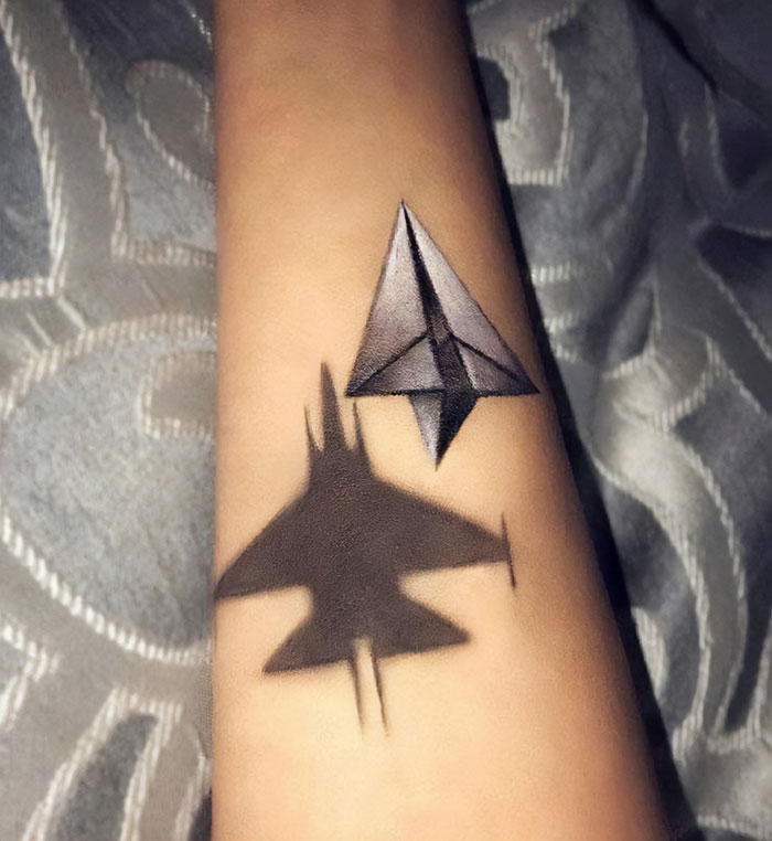 First tattoo idea of a paper plane with a fighter jet shadow, showcasing a creative design on an arm.