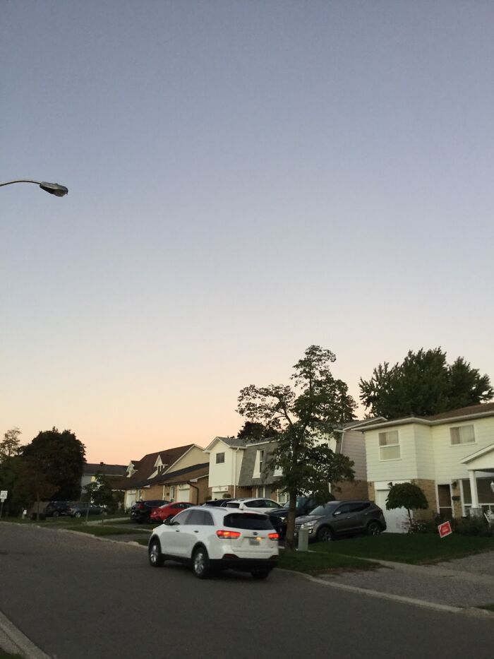 Suburban neighborhood under clear September sky with light traffic and trees during calm weather.