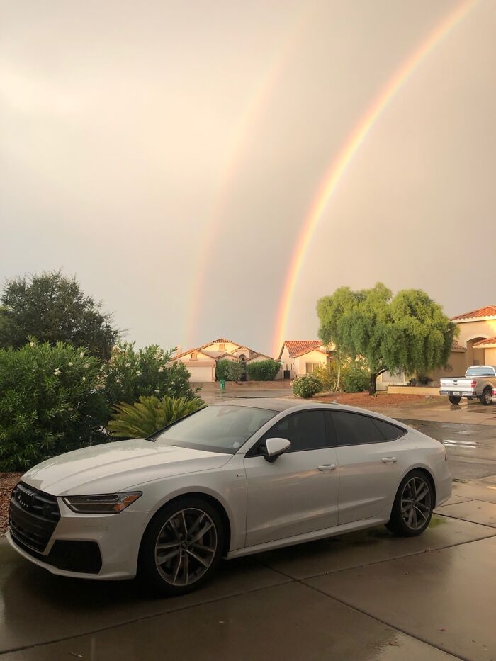White Audi parked on wet driveway with double rainbow in the sky, capturing September weather scenery.
