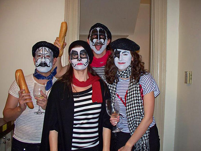 Group of people in easy Halloween costumes with mime face paint, berets, and striped shirts holding baguettes and wine glasses.