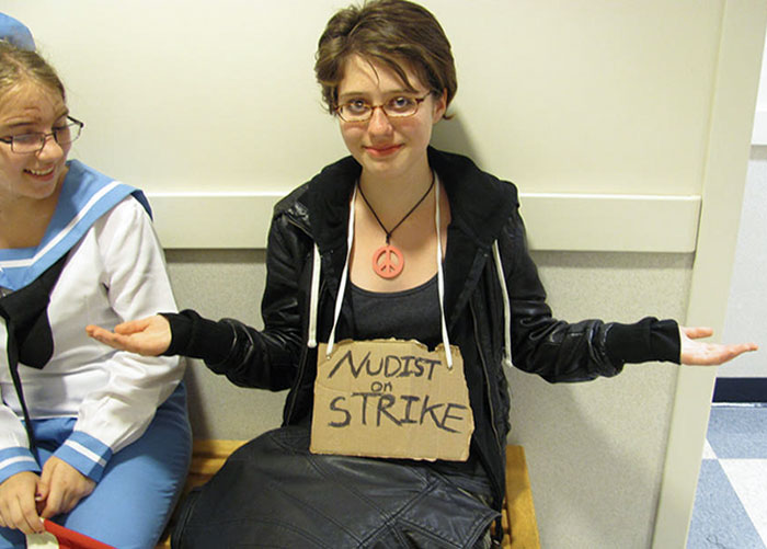 Person in a simple Halloween costume with a cardboard sign saying nudist on strike, showing a low-effort but great costume idea.