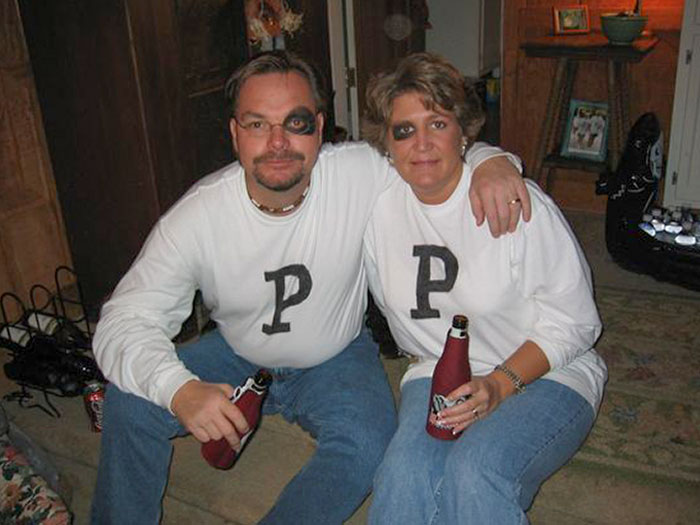 Couple wearing matching simple Halloween costumes with white shirts marked P and black eye patches, holding drinks.