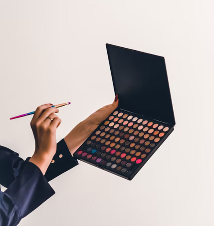 Hands holding a makeup palette and brush, illustrating the concept of pretty privilege in beauty and appearance.
