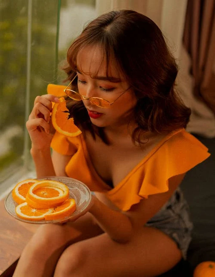 Young woman wearing yellow top and glasses holding orange slices, illustrating the concept of pretty privilege in a casual setting.