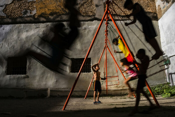 Children playing on a swing set at night, captured in a powerful moment from the 2021 Siena International Photo Awards.
