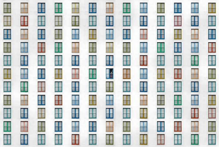 Rows of colorful windows on a white building facade with one person visible, featured in Siena International Photo Awards.