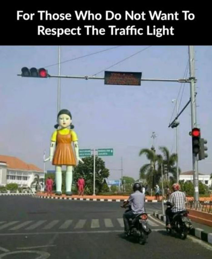 Squid Game doll meme humor, oversized figure at traffic light in city intersection, capturing the show's viral appeal.