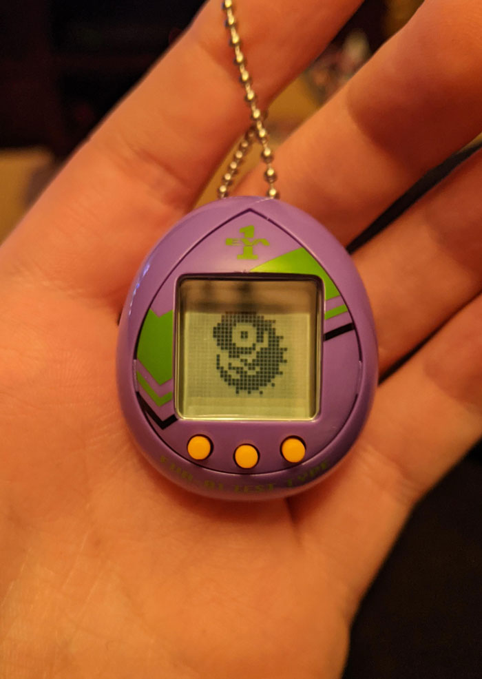 Hand holding a purple Tamagotchi, a nostalgic 2000s digital pet device.