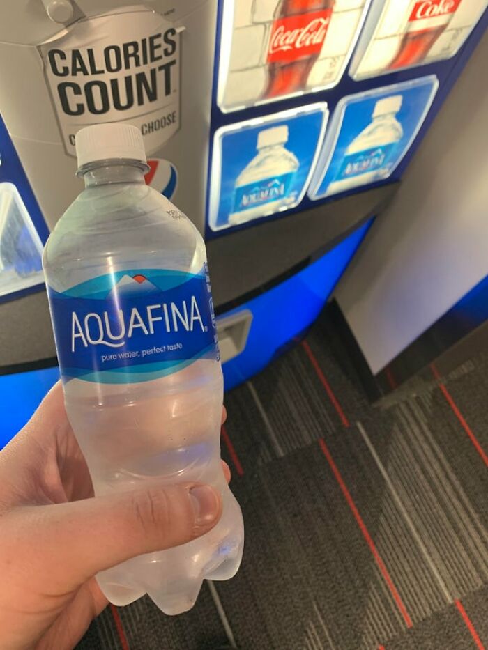 Hand holding a bottle of Aquafina water near a vending machine, highlighting drinking water choices.