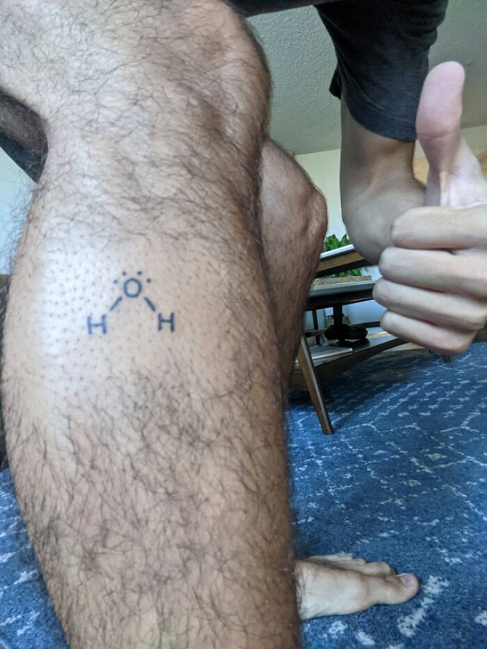 A leg with a tattoo of a water molecule and a thumbs-up, humorously highlighting drinking water.
