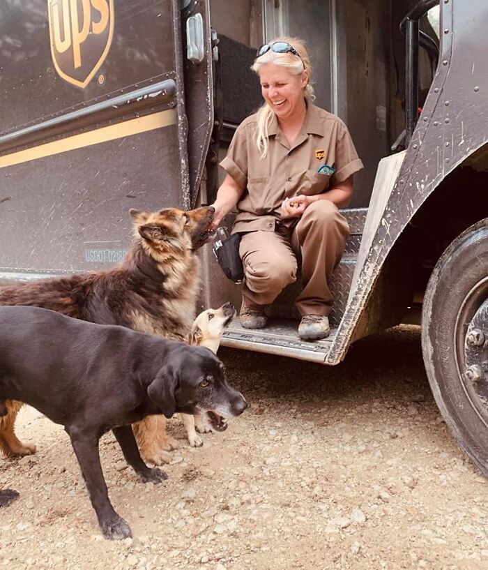 UPS driver smiling and interacting with dogs on her delivery route outside a UPS truck.