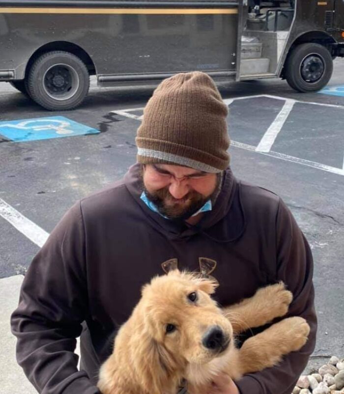 UPS driver smiling while holding a friendly golden retriever dog during delivery route in parking lot.