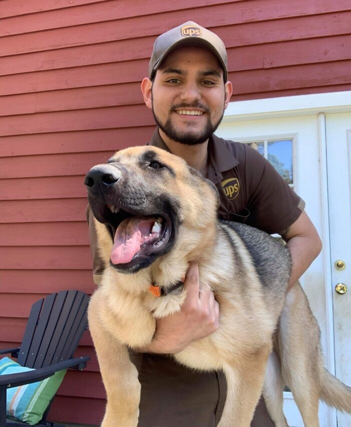 UPS driver smiling and holding a large happy dog met on his delivery route for a Facebook group about dogs.