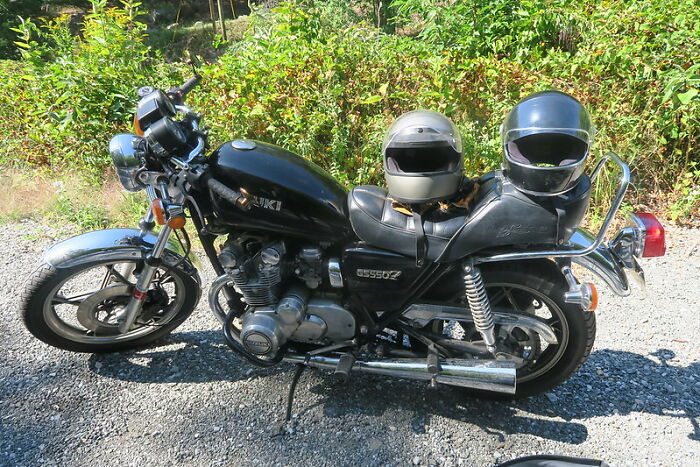 Black Suzuki motorcycle parked on gravel with two helmets, illustrating a product completely worth your money.