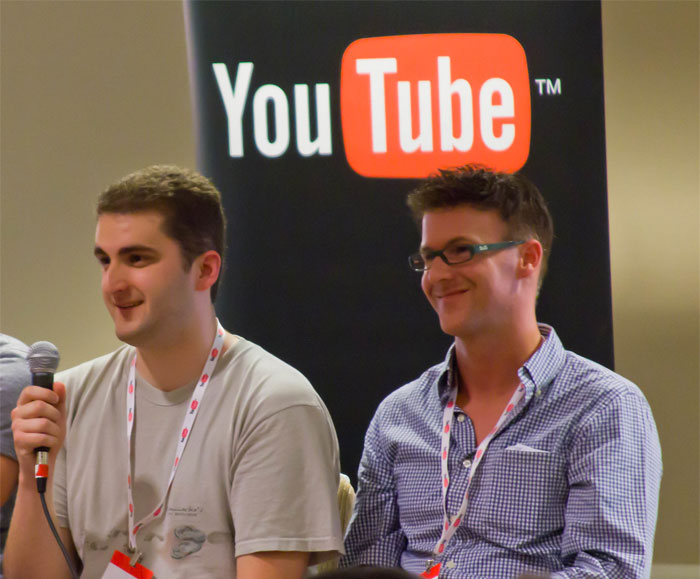 Two men sitting and speaking with a YouTube logo behind, related to sarcastically honest brand slogans discussion.
