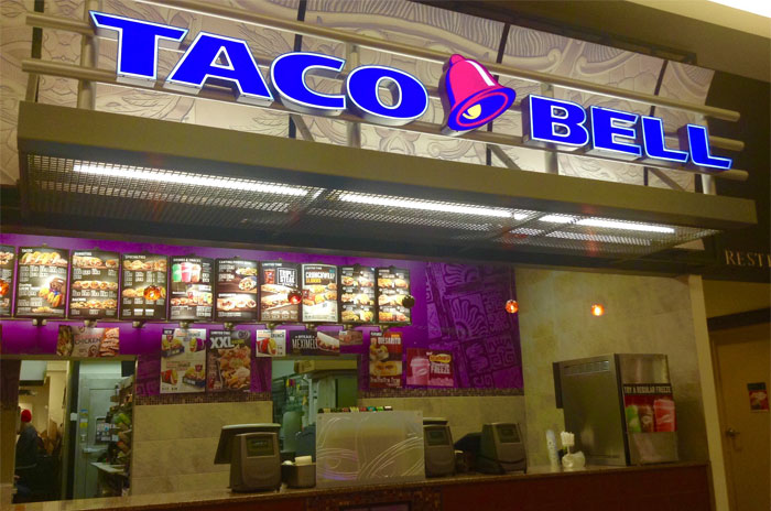 Taco Bell fast food counter with illuminated sign and menu boards showcasing sarcastically honest brand slogans.