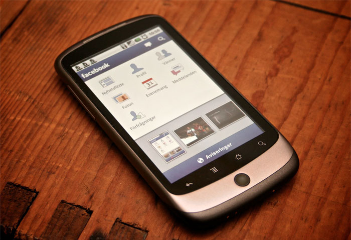 Smartphone displaying Facebook app interface on wooden surface, illustrating sarcastically honest slogans about famous brands online.