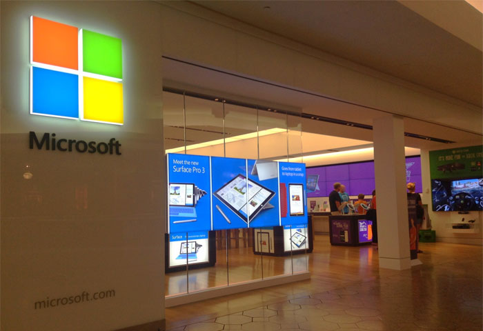 Microsoft store storefront with digital displays and people inside illustrating sarcastically honest slogans about famous brands.