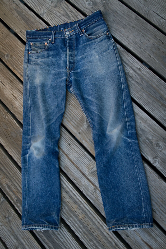Faded blue jeans laid flat on wooden deck showcasing worn details in a casual product worth the money.
