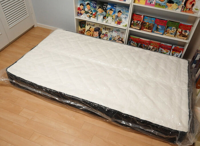 Mattress wrapped in plastic on a wooden floor with shelves of graphic novels in the background, product worth the money