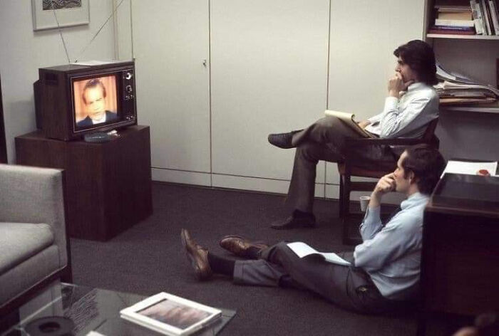 People watching an important historical moment on a vintage TV in an office setting.