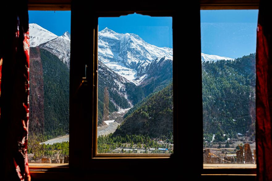 Beautiful scenery of snow-capped mountains and lush forest viewed through a window.