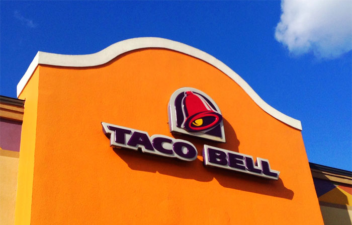 Taco Bell restaurant exterior with logo on orange wall under clear blue sky, illustrating sarcastically honest brand slogans.