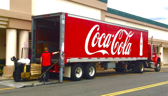 Red Coca-Cola delivery truck being unloaded by a worker, illustrating sarcastically honest slogans about famous brands.