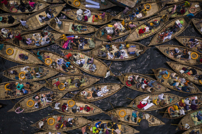 Aerial view of crowded wooden boats filled with people on dark water showcasing environmental photographer of the year 2021.