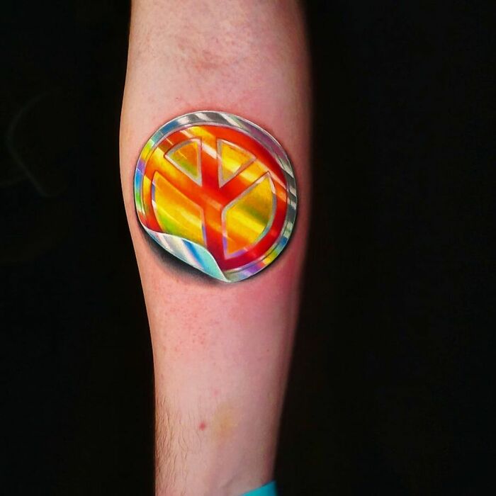 Brazilian artist's tattoo resembling a holographic sticker on an arm, featuring a vibrant peace symbol design.