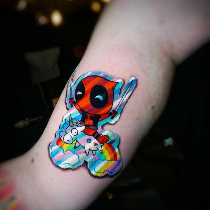 Holographic sticker style tattoo of a cartoon superhero riding a unicorn on a rainbow.