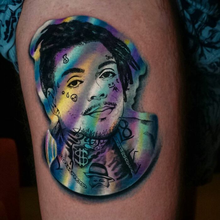 Holographic sticker-style tattoo of a person's face with colorful, reflective effects created by a Brazilian artist.