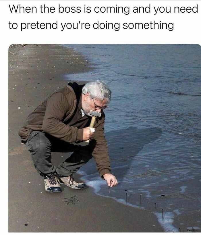 Man pretending to work by hammering nails into wet sand on a beach, illustrating work-related memes humor.