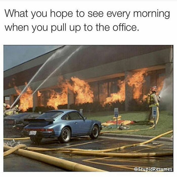 Burning office building with firefighters spraying water and a blue car parked outside, a work-related meme about office chaos.