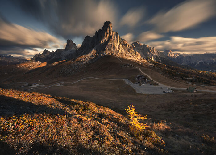 Mountain landscape in the Alps during colorful fall, showcasing rocky peaks and autumn foliage under dramatic skies.