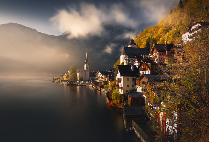 Scenic mountain village by a lake in the Alps during colorful fall with mist and autumn foliage at sunrise.