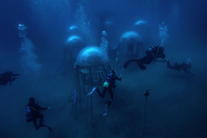 Underwater divers exploring transparent dome structures on the ocean floor, highlighting environmental photographer of the year subjects.