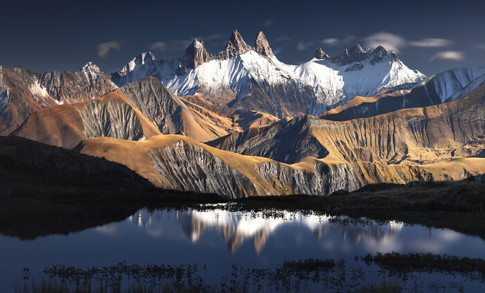 Snow-capped Alps mountains reflecting in a lake during colorful fall, captured by a mountain photographer.